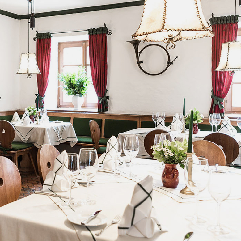 Elegant dining room with tables set for a meal, featuring white tablecloths, red curtains, and hanging lamps.