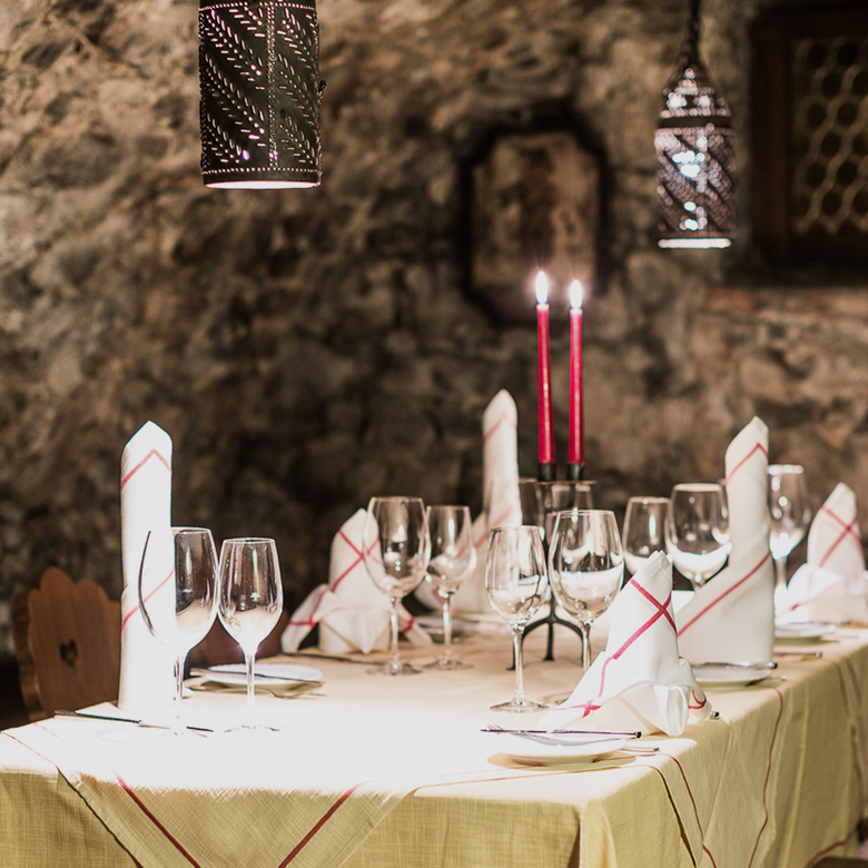Elegant dining table set with white linens, wine glasses, and lit pink candles in a rustic stone wall room.