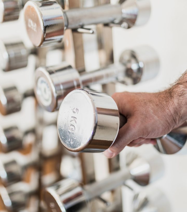 A hand reaches to select a shiny chrome 5KG dumbbell from a rack of weights.